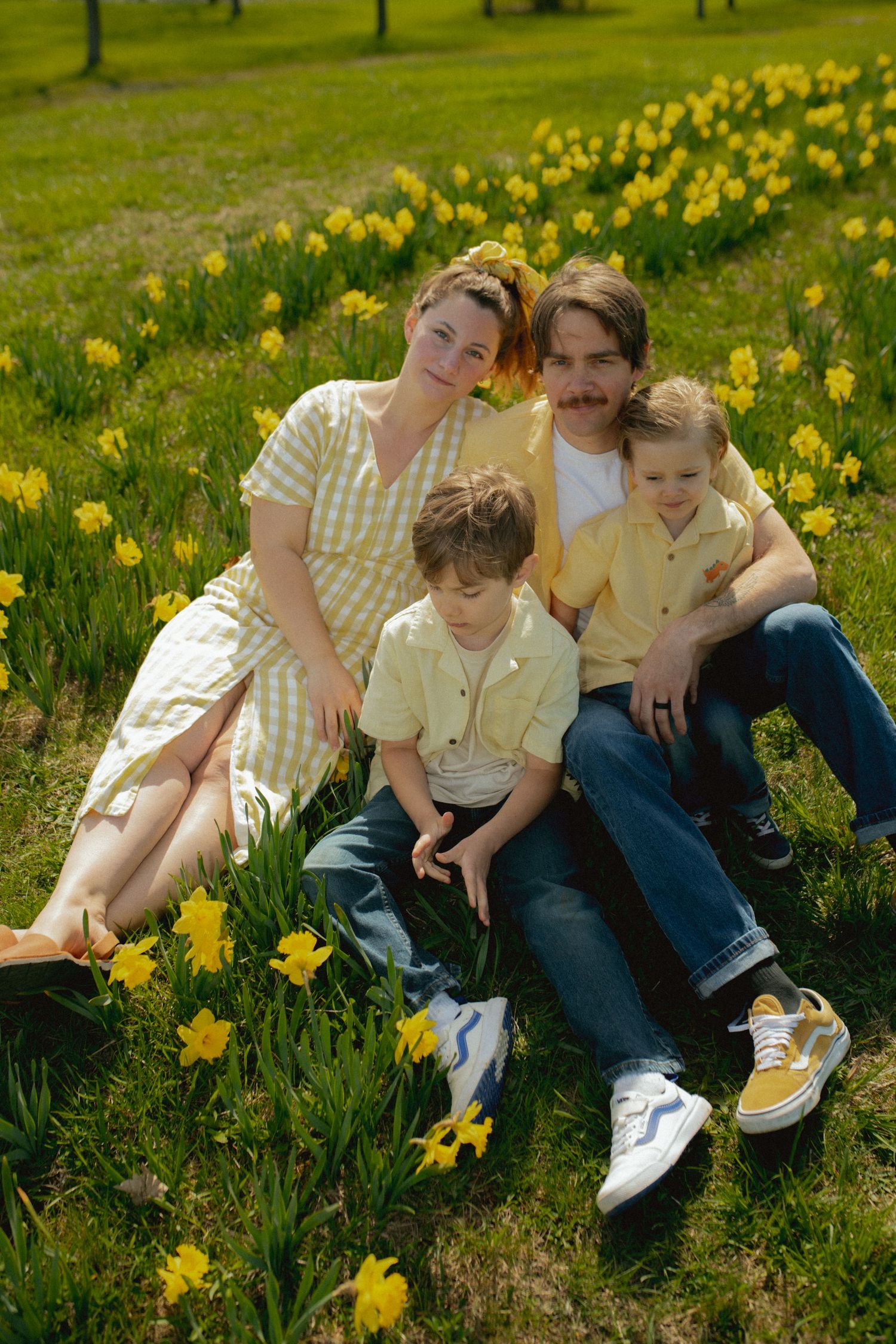 A family sits together in a field of blooming yellow daffodils on a sunny spring day.