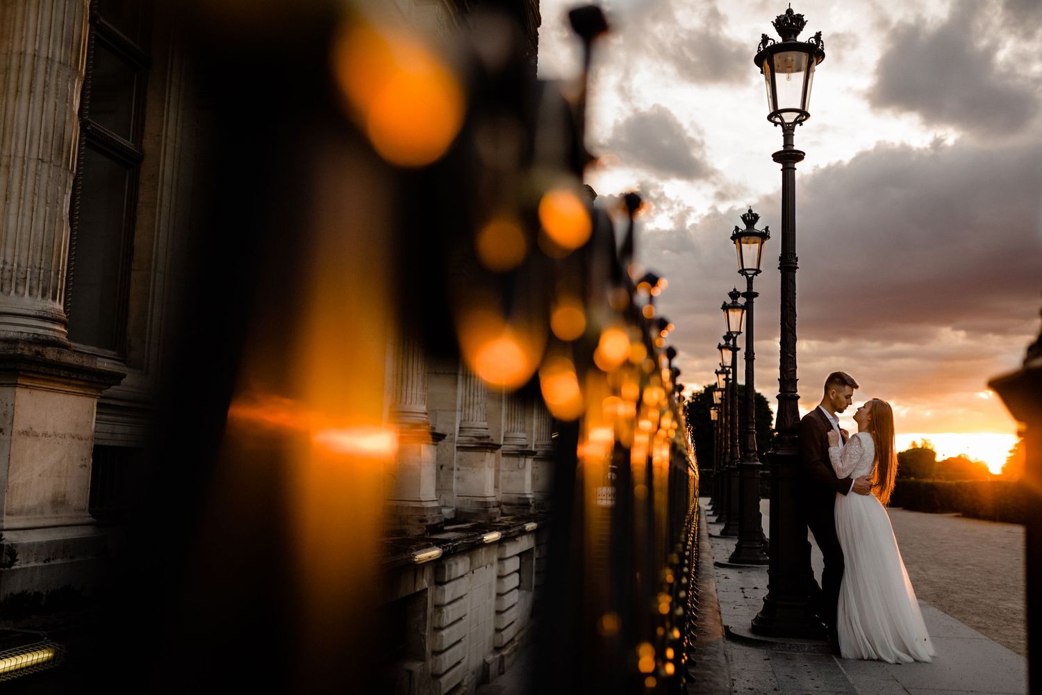 Couple embracing at sunset near ornate lamp posts outside a grand Parisian building during a romantic wedding photo session.