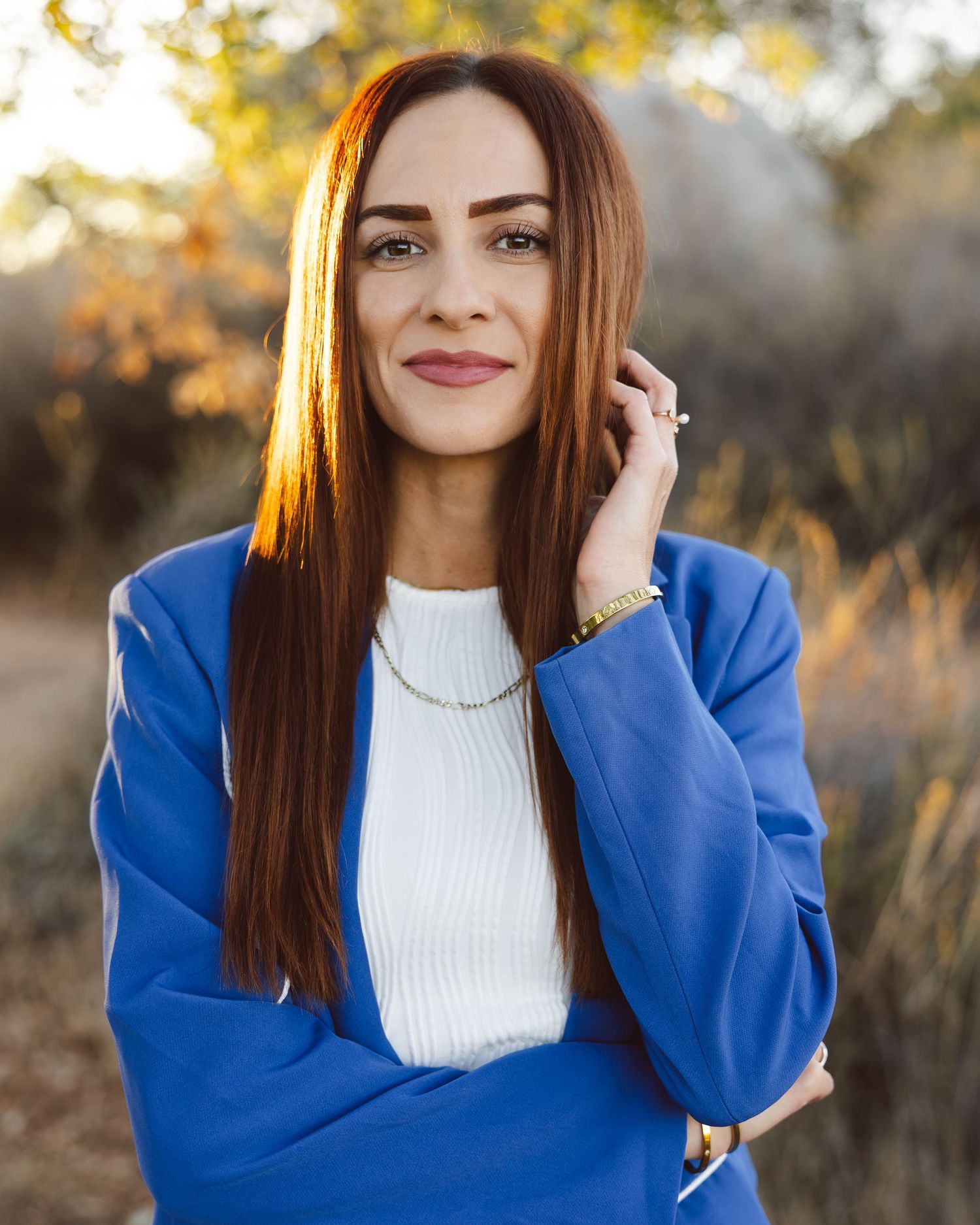 Portrait of someone in a bright blue cardigan and white top against an autumn background with golden sunlight.