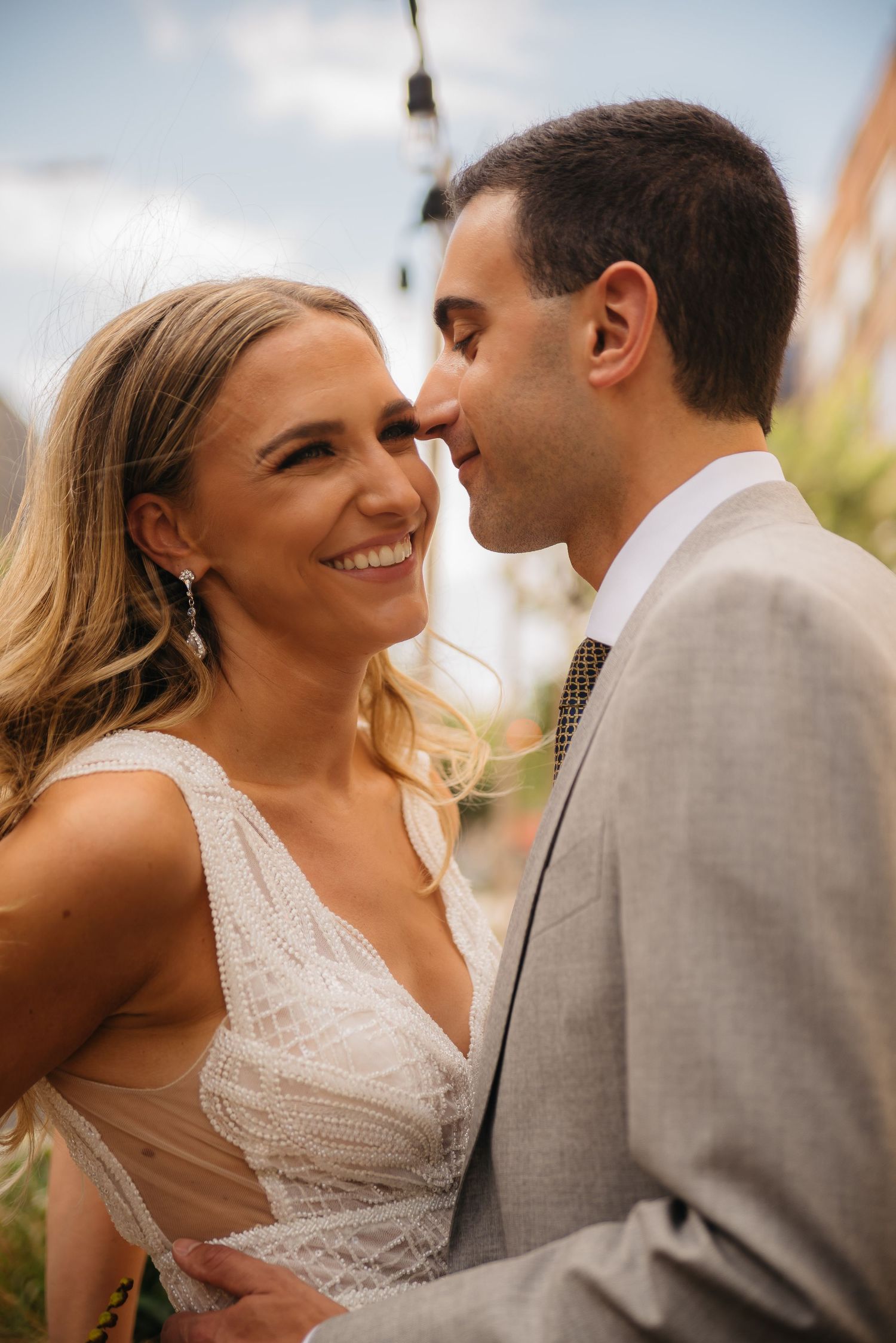 Candid moment of newlyweds sharing an intimate moment outdoors, bride in white lace dress and groom in grey suit.