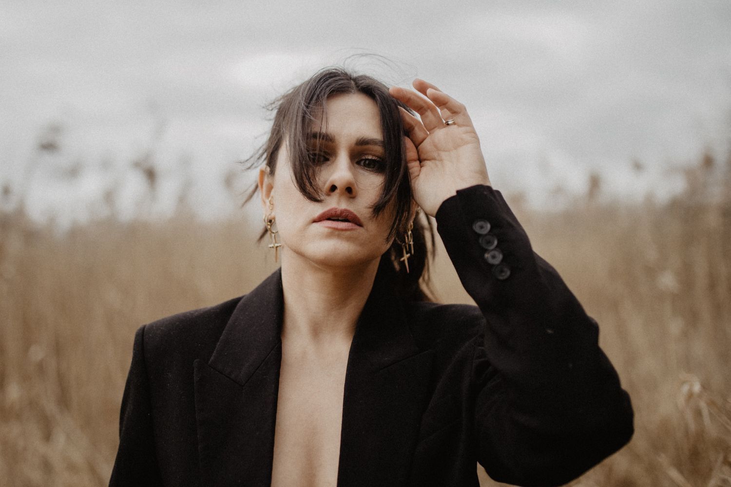 Artistic portrait of a person in black blazer with wind-swept hair against natural backdrop.