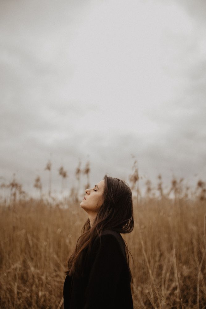 Figure standing in brown field gazing up at cloudy sky.