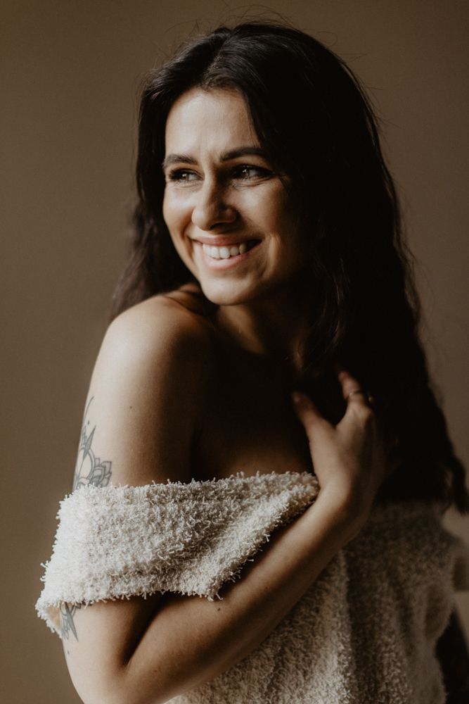 Portrait in soft lighting shows off-shoulder sweater and natural expression.
