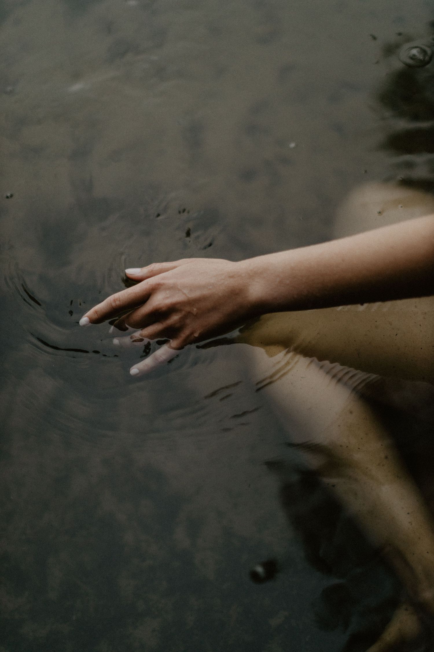 Hand reaching into dark rippling water creating subtle reflections and movement.