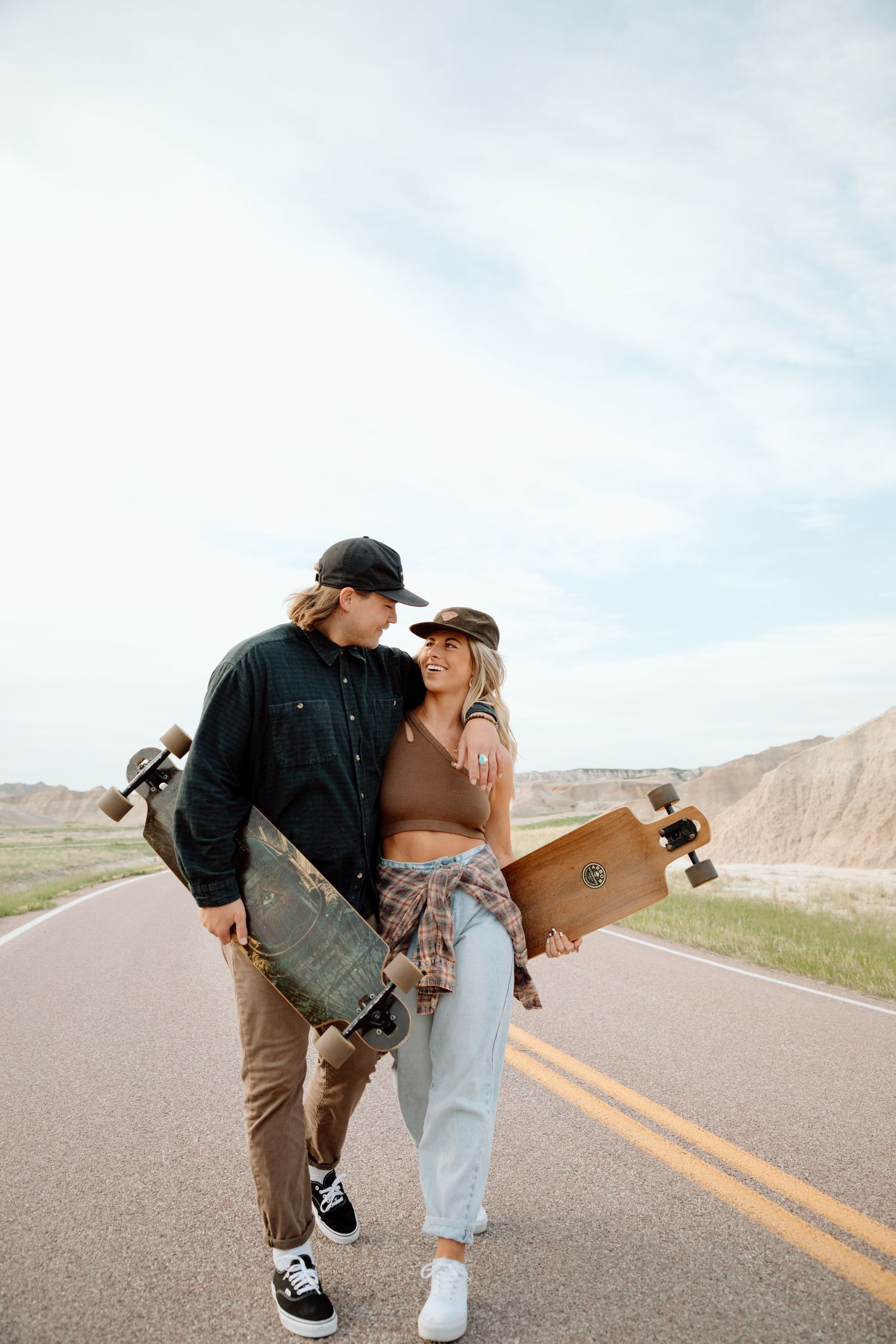 Couple in casual attire sharing playful moments on empty desert road.