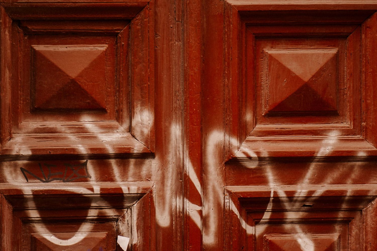 Close-up of graffiti tags spray painted on red wooden door panels.