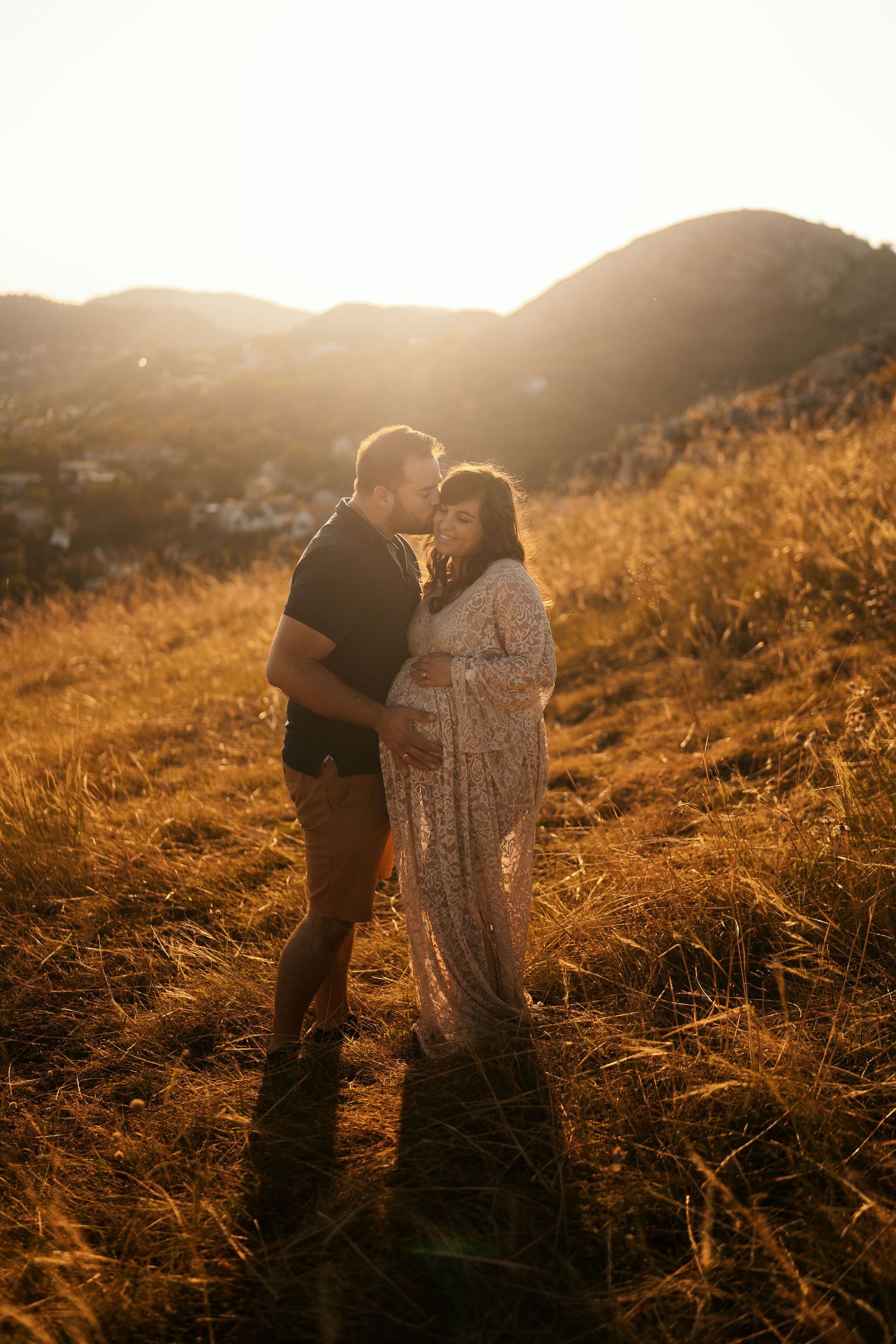 Couple embracing in golden sunset light on grassy hillside.