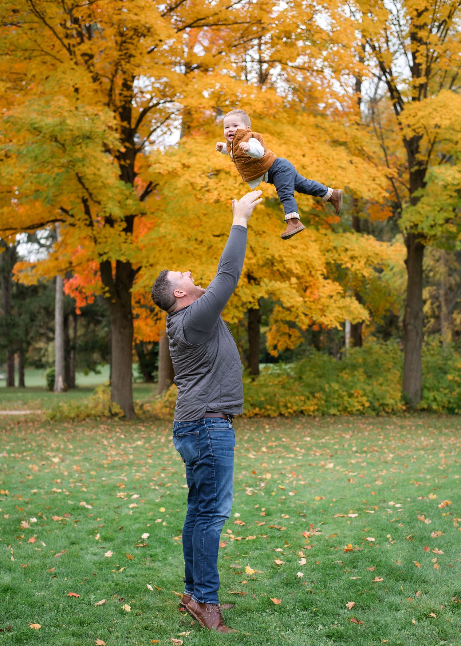 Playful moment as adult lifts child high in the air against golden autumn trees.