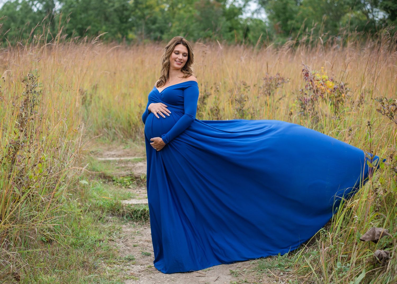 Pregnant woman in flowing blue dress poses in autumn field.