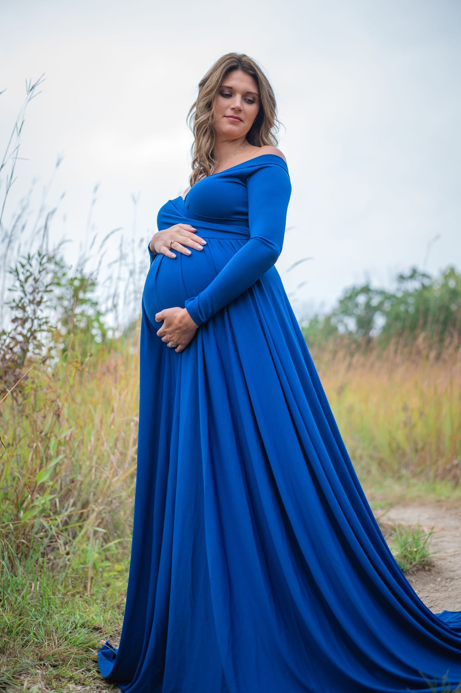 Expecting mother in royal blue gown poses in golden field.