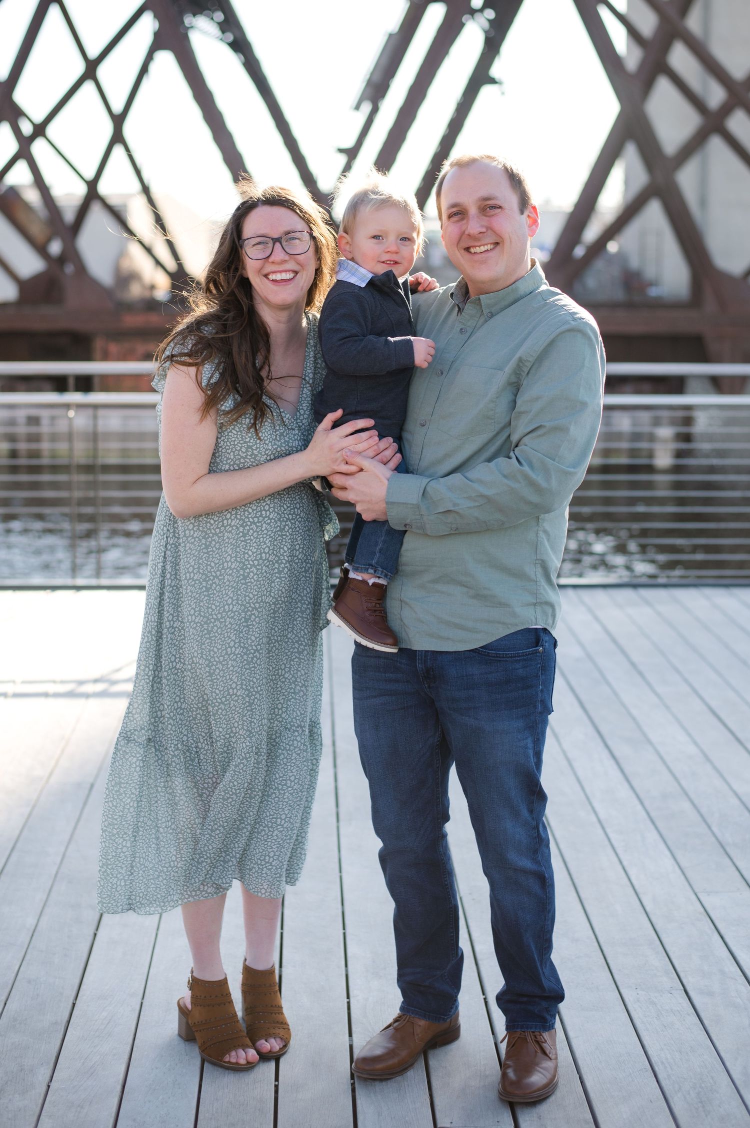Family portrait on wooden bridge with industrial metal structure in background.