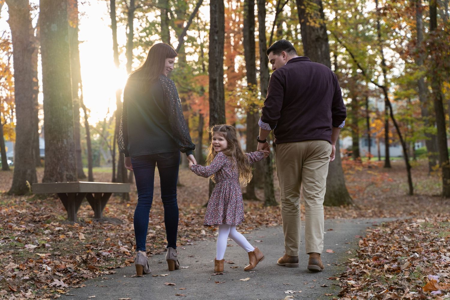 Family walks together on path through autumn woods with golden sunlight filtering through trees.