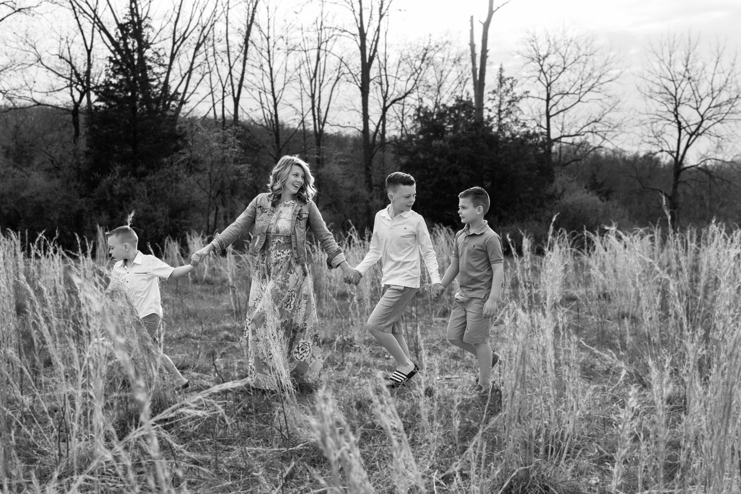 Black and white photo of family walking through tall grass field.