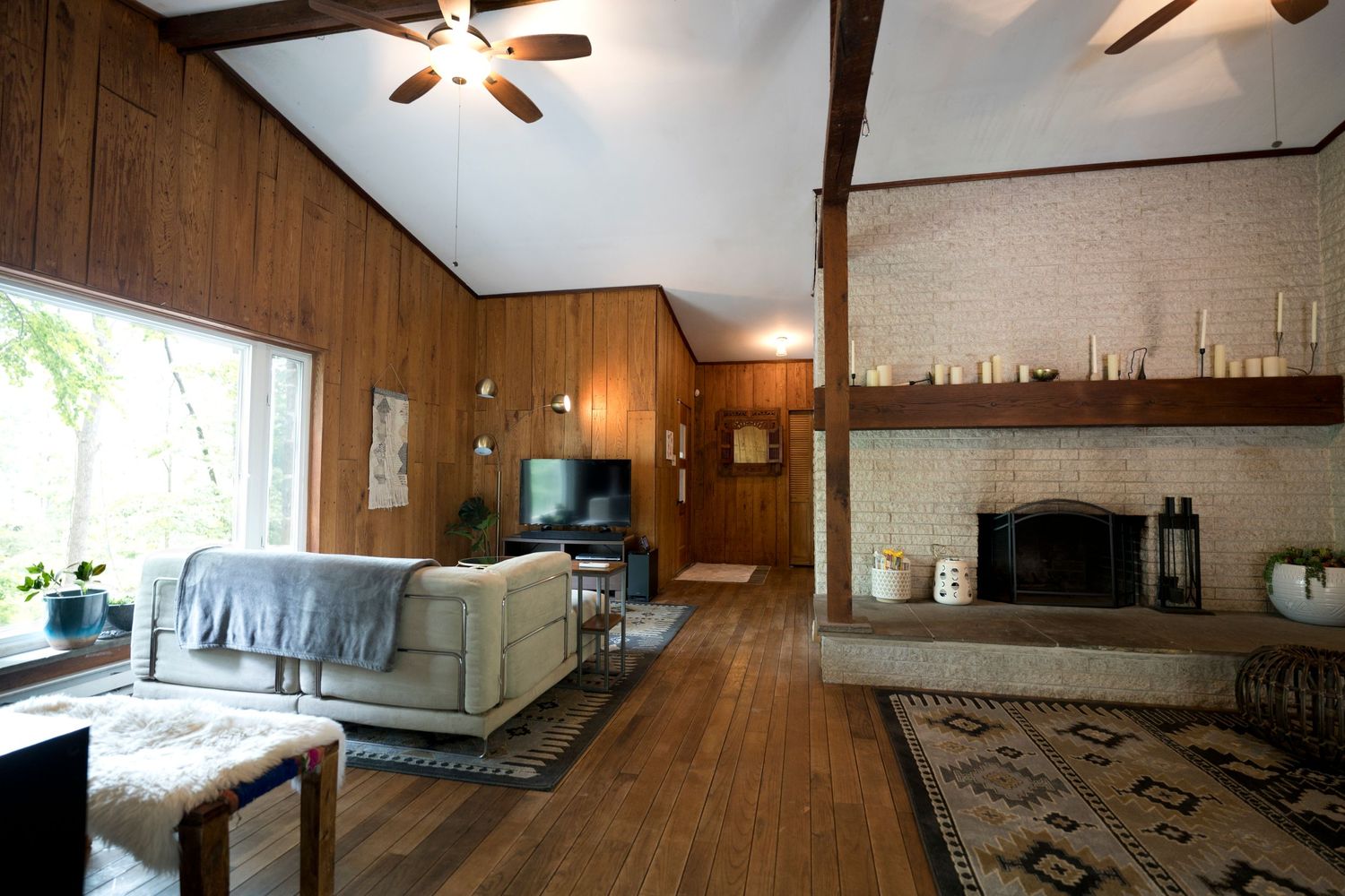 Rustic living room with wood paneling, ceiling fans, and a stone fireplace.
