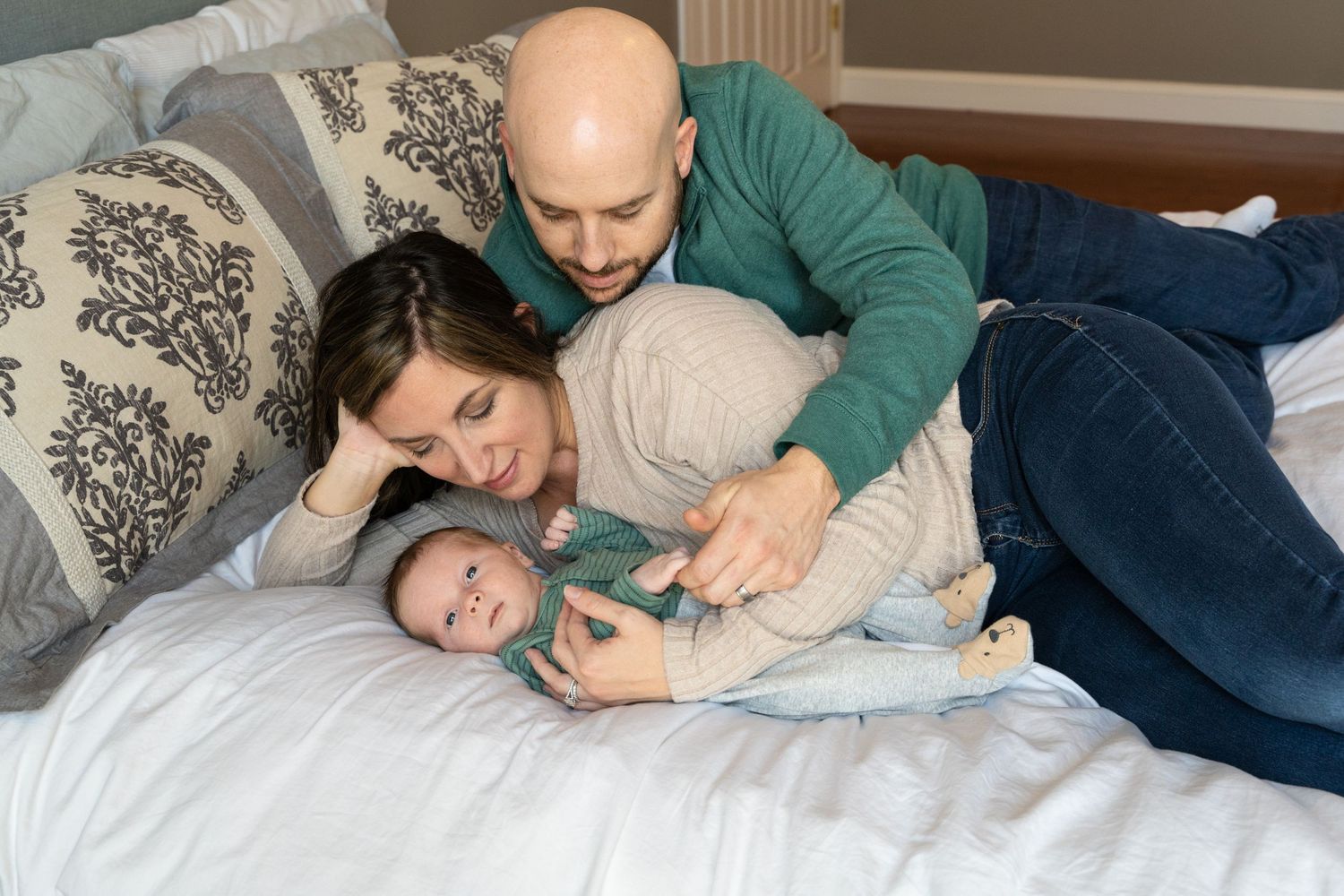 Sweet family moment captured on white bed with patterned cushions.