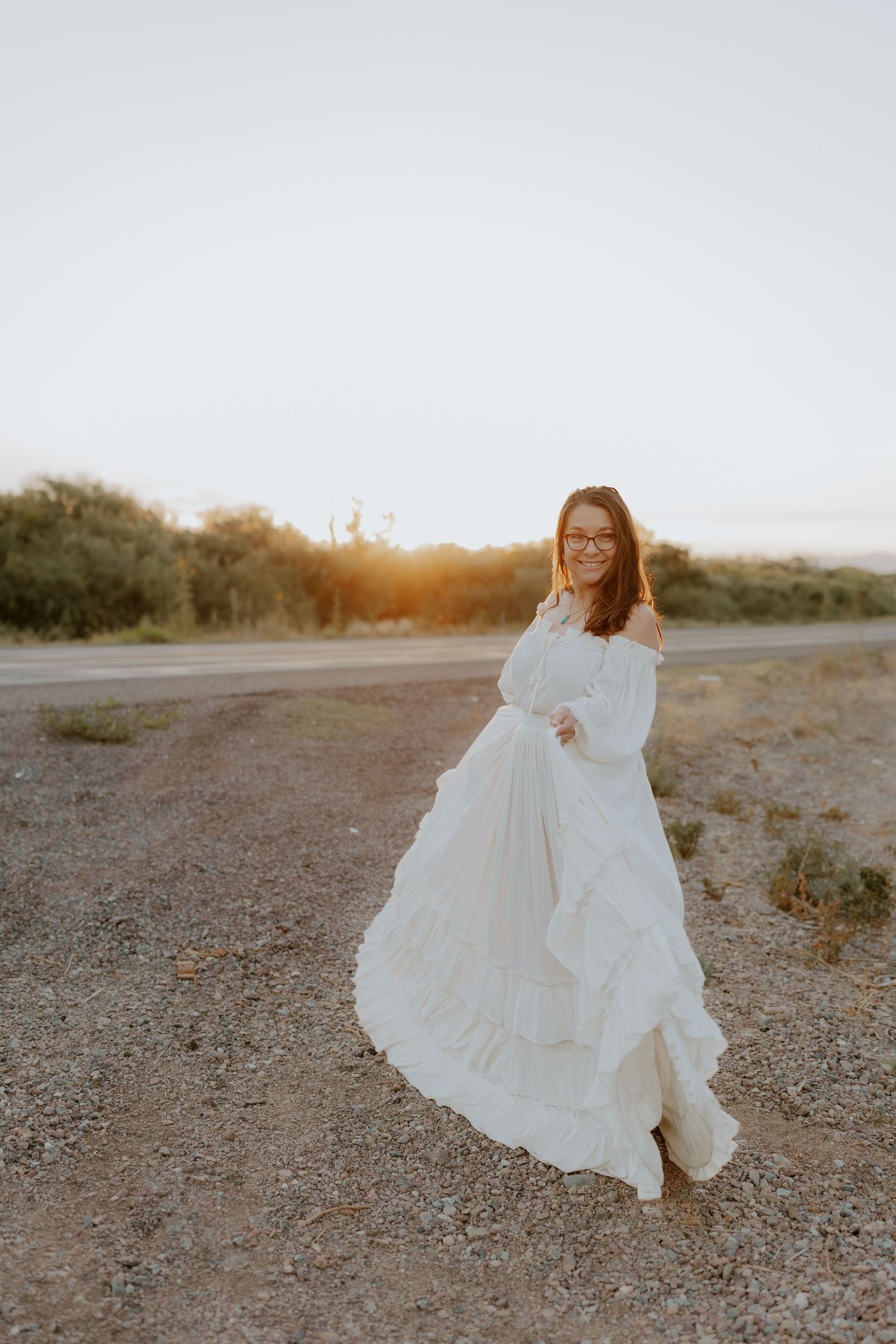 Woman in flowing white dress twirling in desert landscape during sunset.