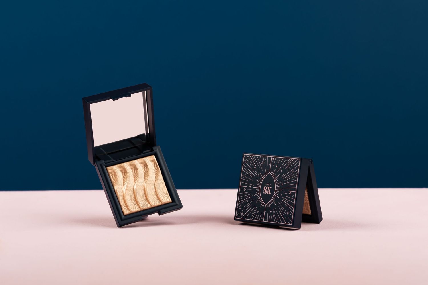 Two decorative black compact cases displayed on a pink surface against a navy blue background.