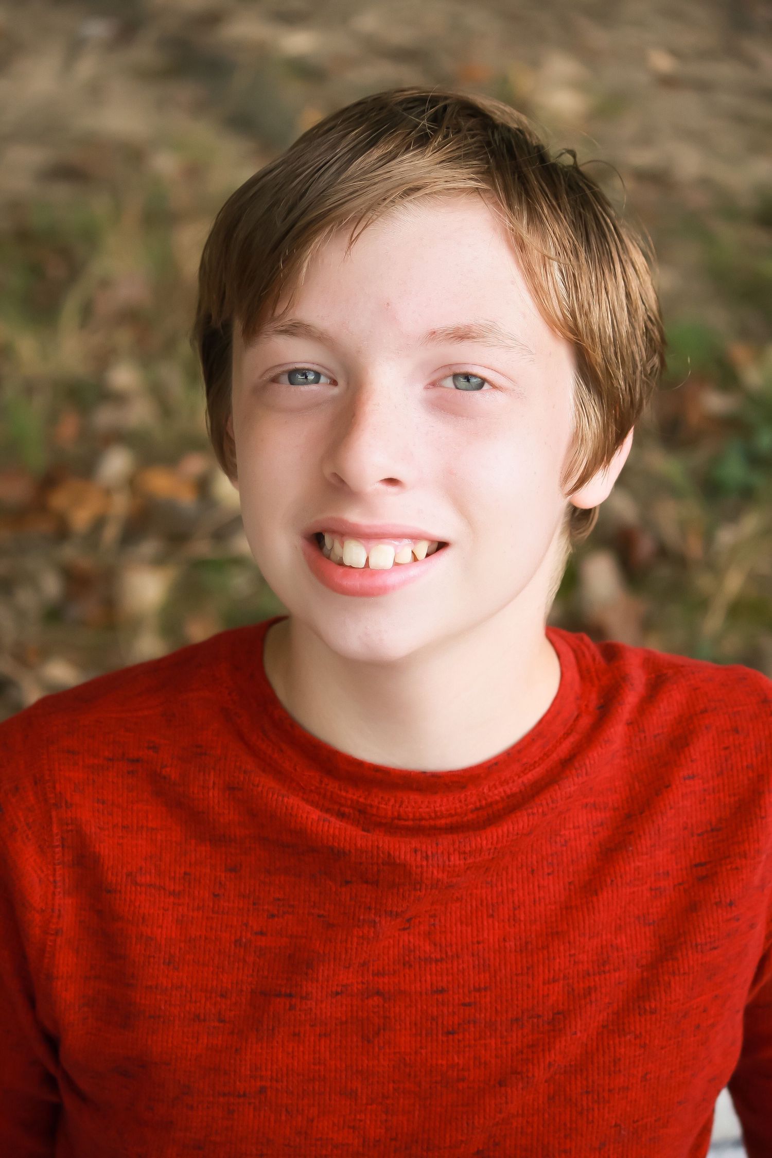 Someone wearing a bright red sweater smiles warmly at the camera in an autumn outdoor setting.