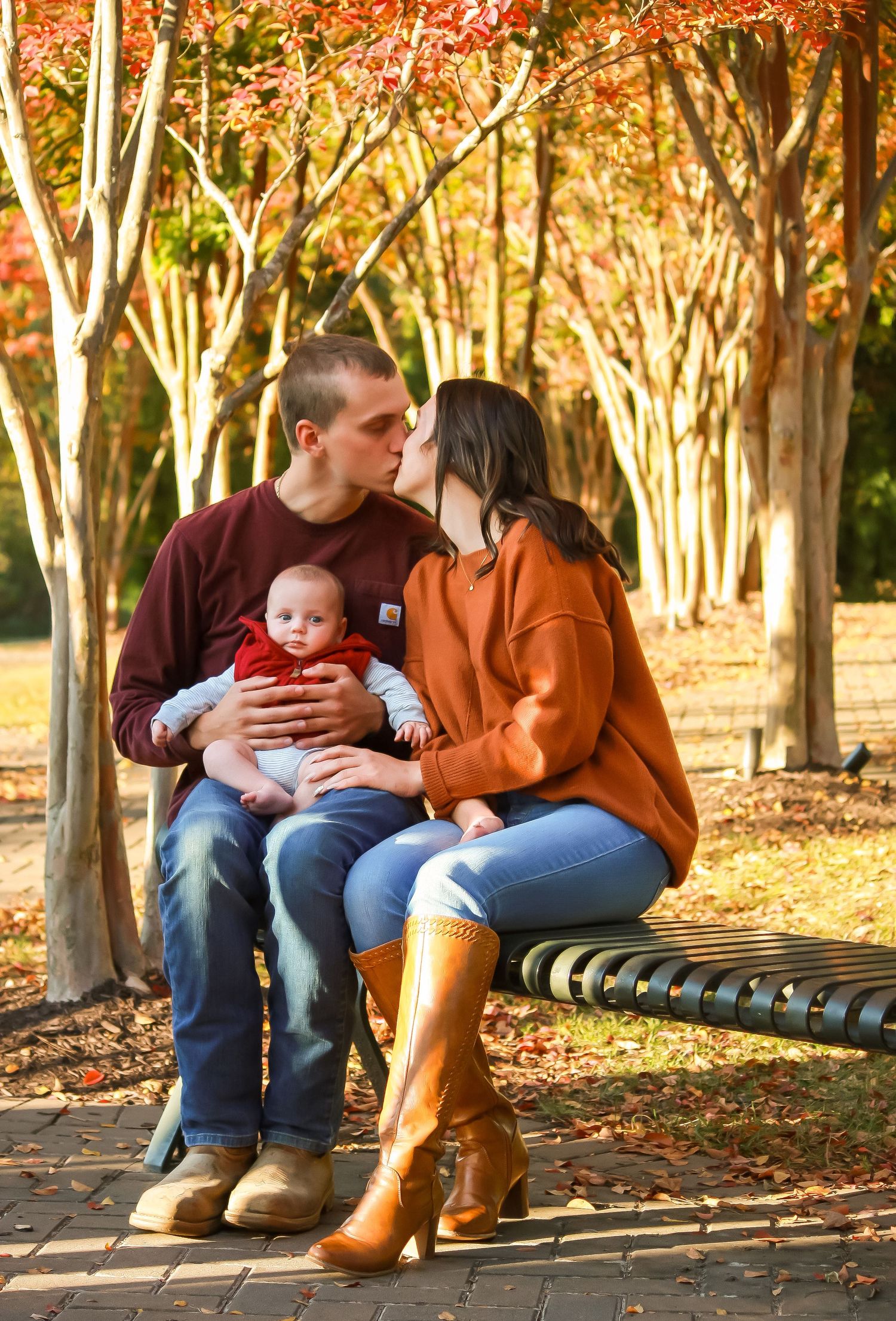 A family shares a quiet moment together on a park bench surrounded by golden autumn trees.