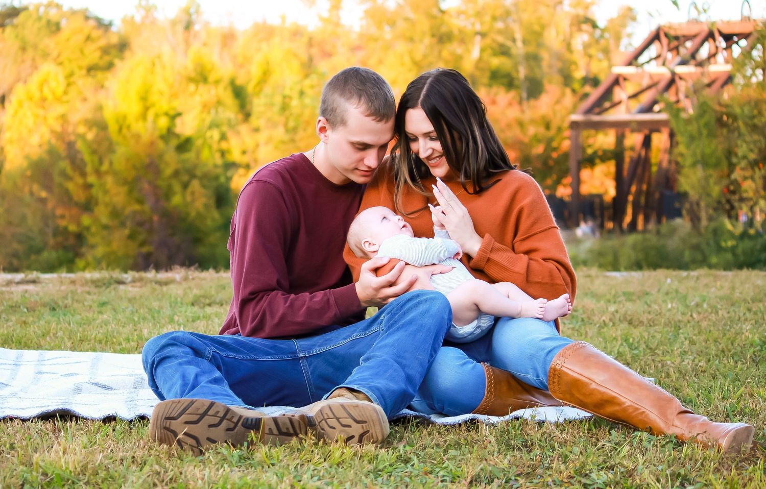 A family sitting together on a blanket in a grassy field during sunset with autumn colors.