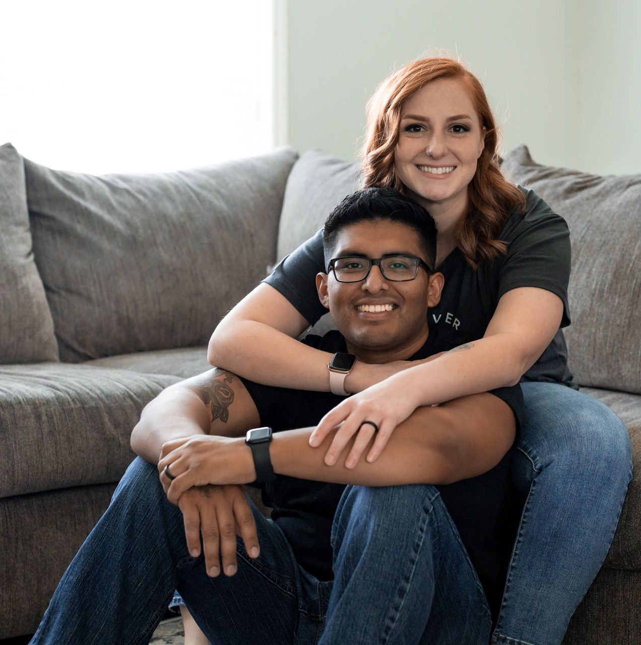 Couple lounging together on grey sofa in bright living room.