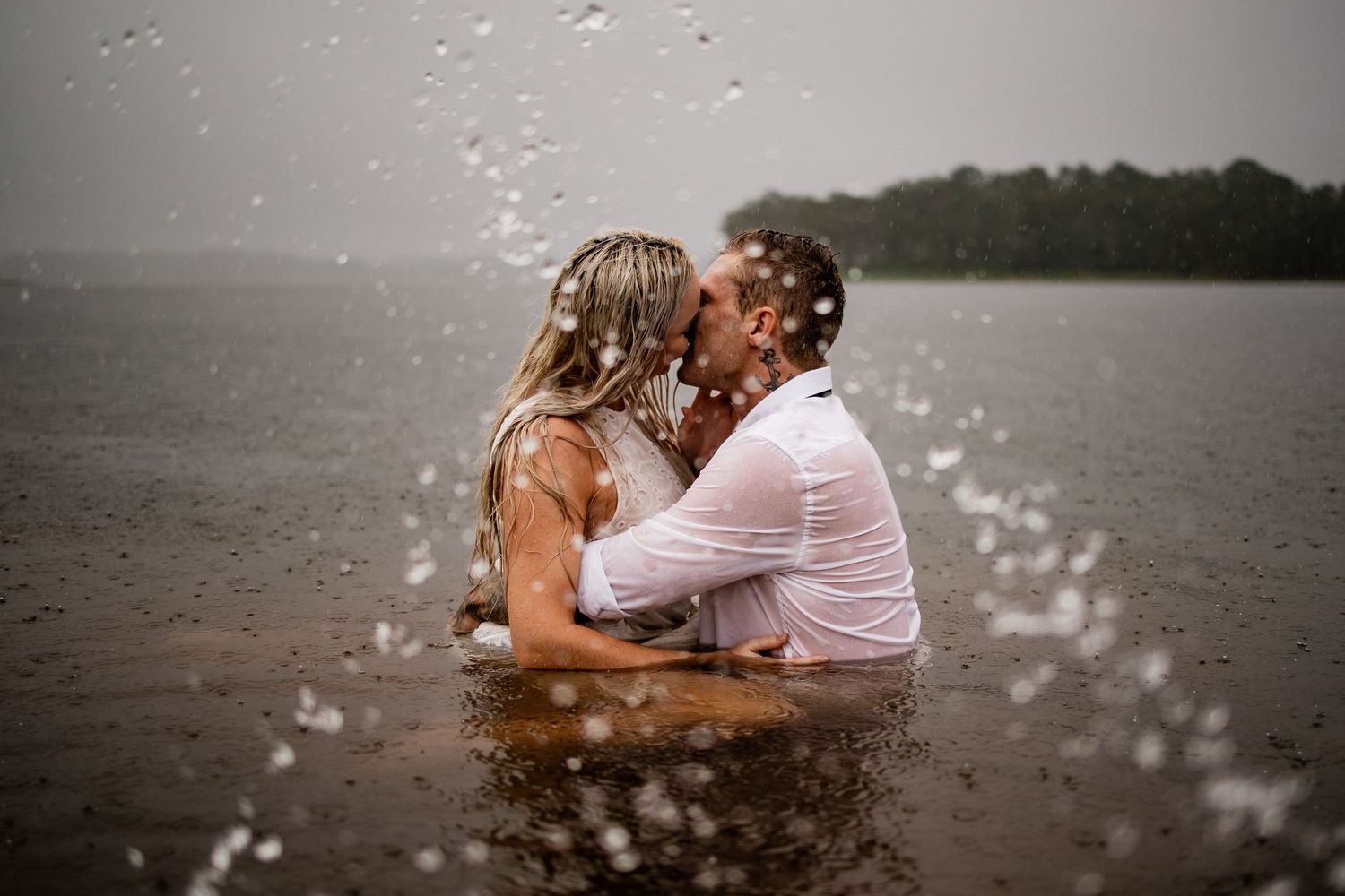 A couple embracing in water with splashes surrounding them during an outdoor photoshoot.