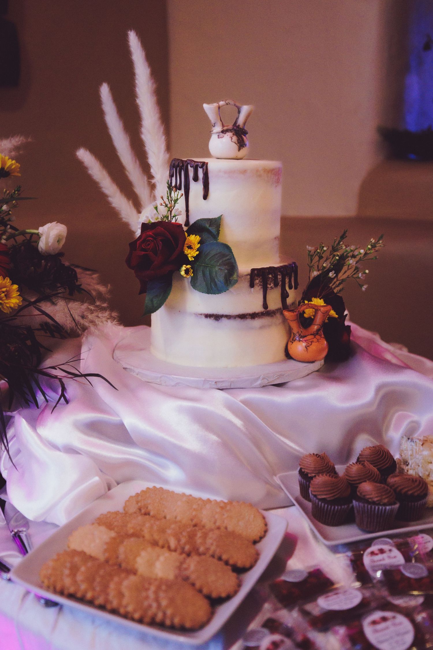 a wedding cake with white frosting and a artful chocolate drizzle, topped with a Native American pot.