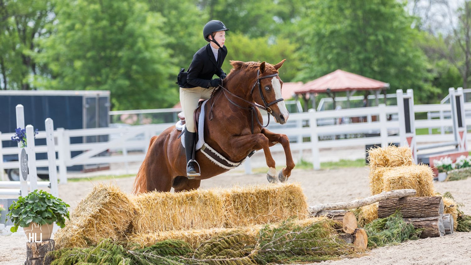 Horse and rider clearing hay bale jump during equestrian competition.