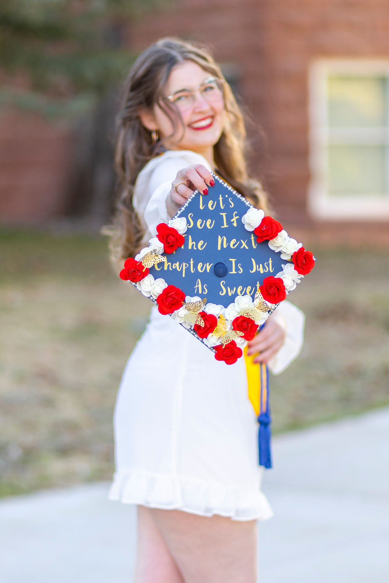 Decorated graduation cap with red flowers and inspirational quote displayed outdoors.