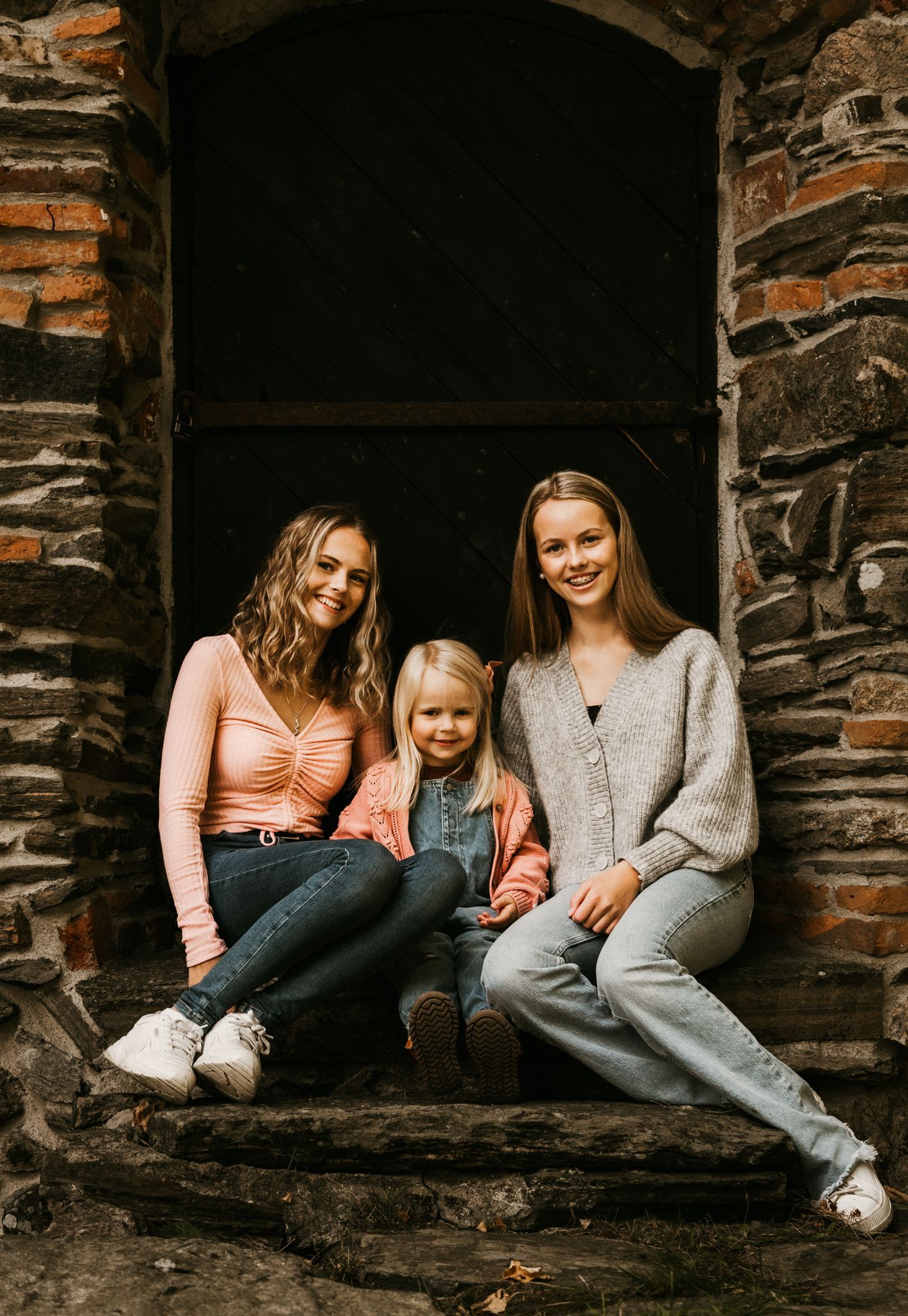 Three people sitting together in a rustic stone archway.