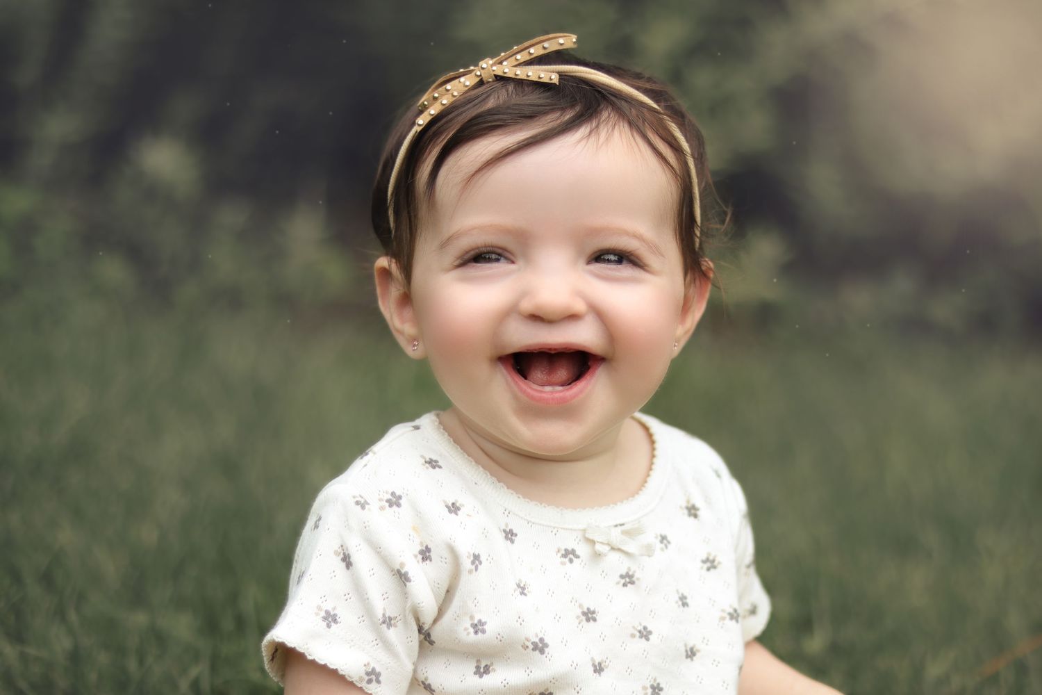 infant girl wearing a gold headband laughing with the sun glow in the background