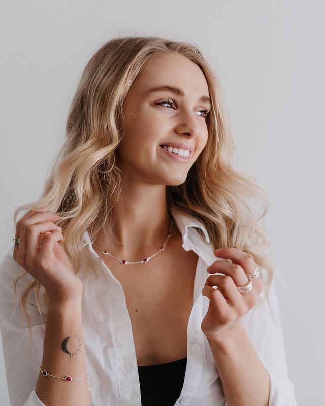 Studio portrait shows a joyful expression while wearing a white button-down shirt and delicate necklace.