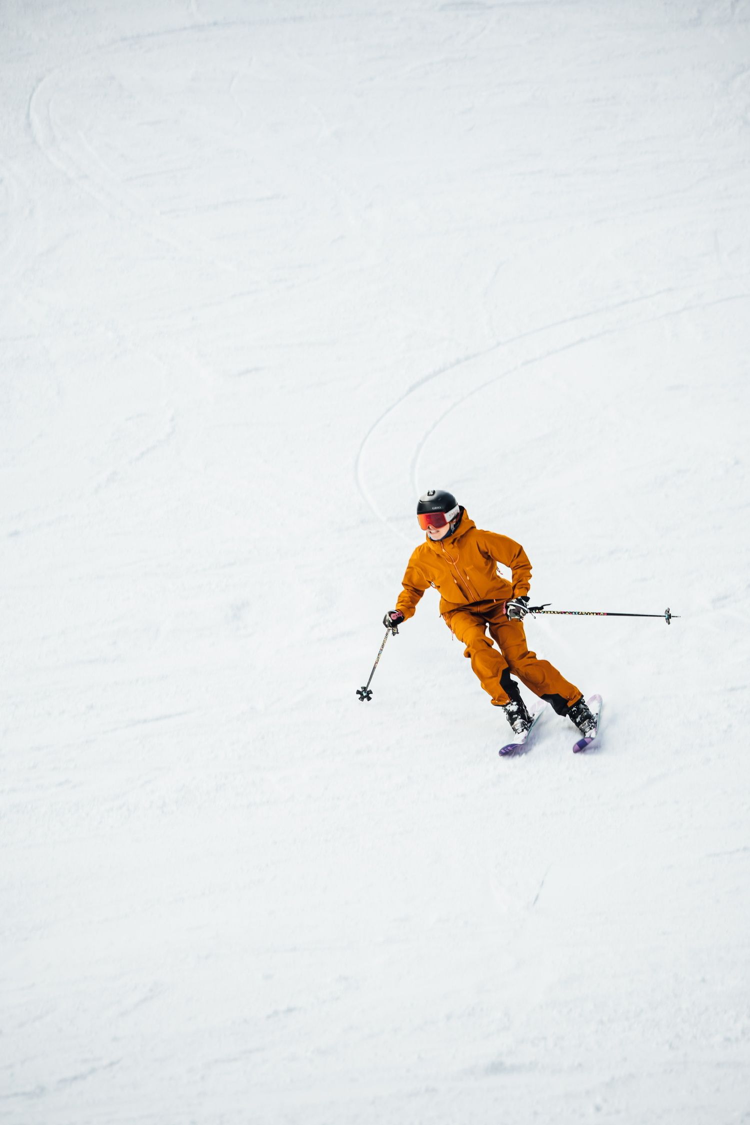 Skier in bright orange suit carving down pristine white snow slope.