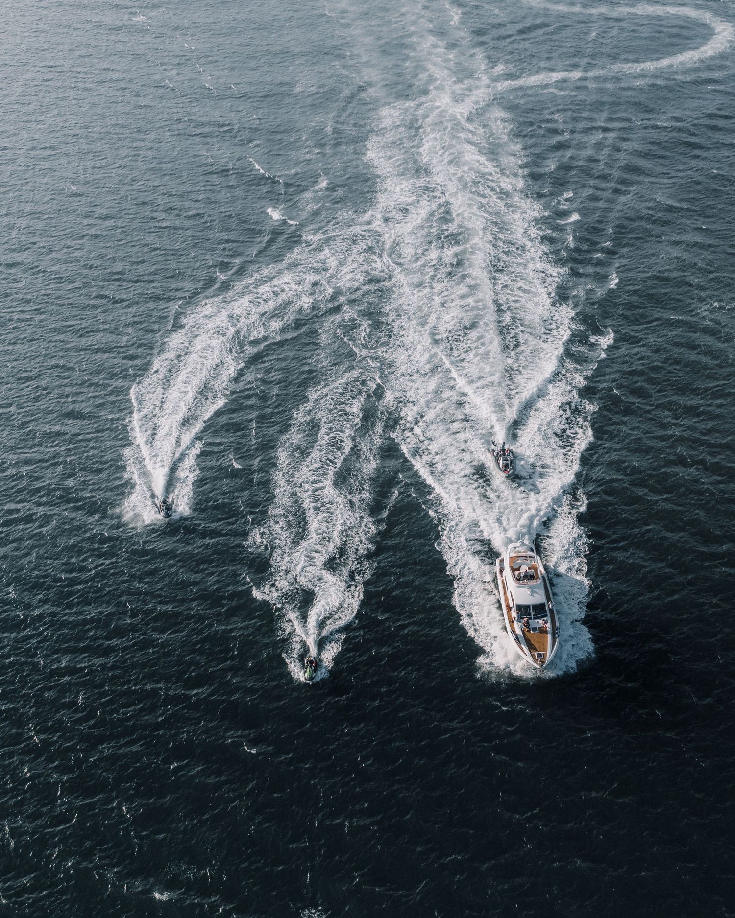 Aerial view of a boat creating dramatic wake patterns in dark blue ocean waters.