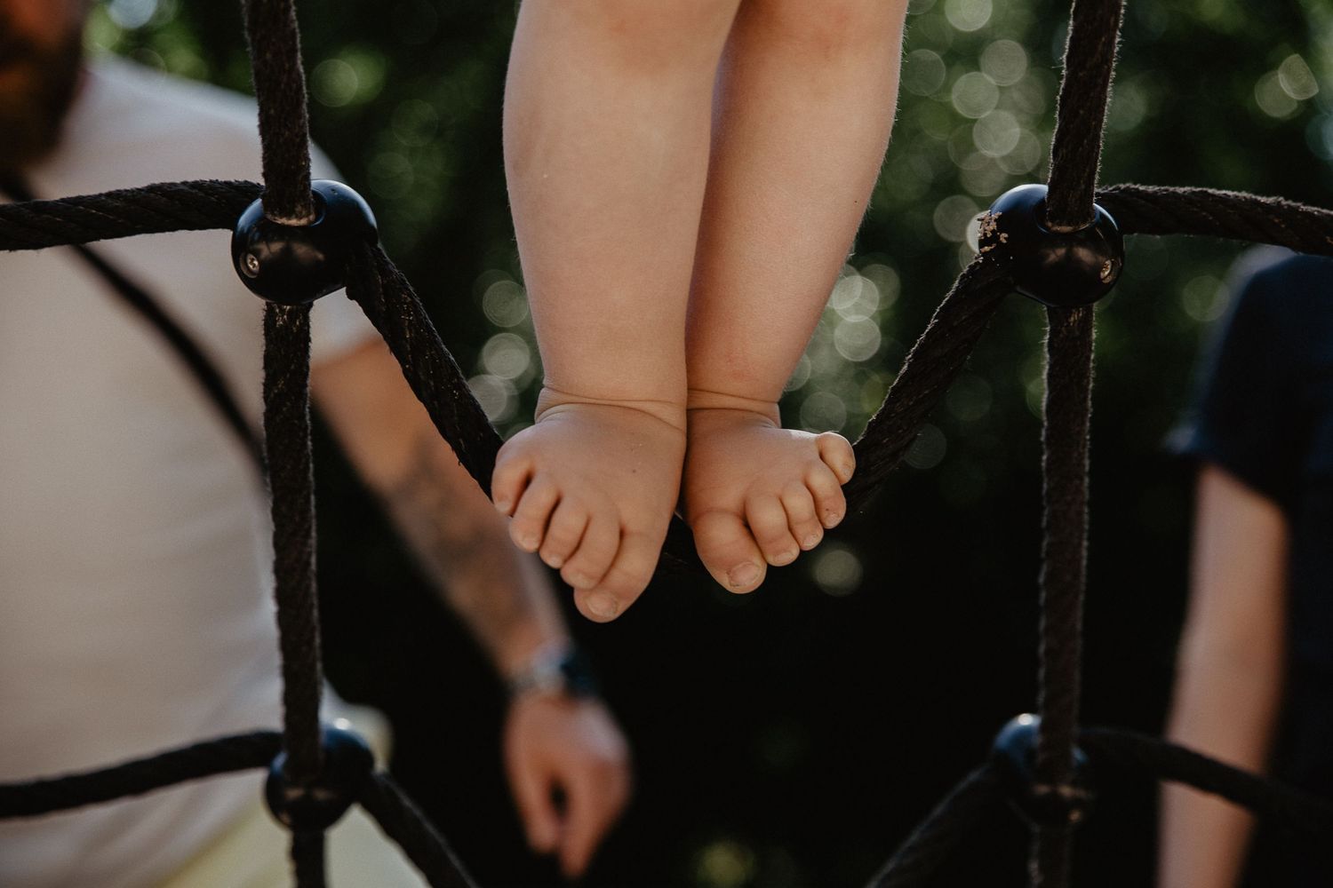 Small bare feet dangling between black metal bars of playground equipment.