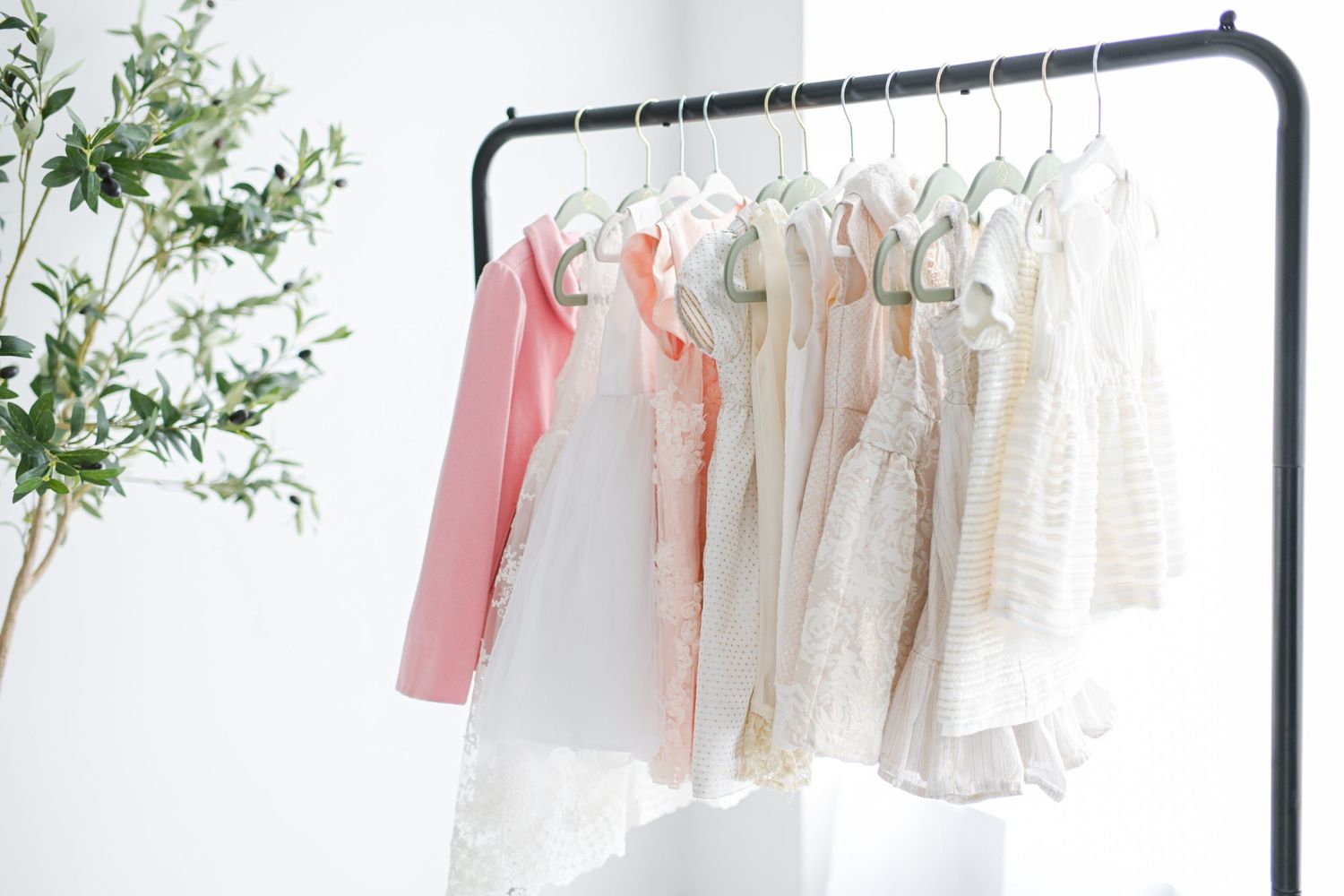 some of the dresses from the little girls wardrobe, on a clothing rack in a studio with olive tree behind them