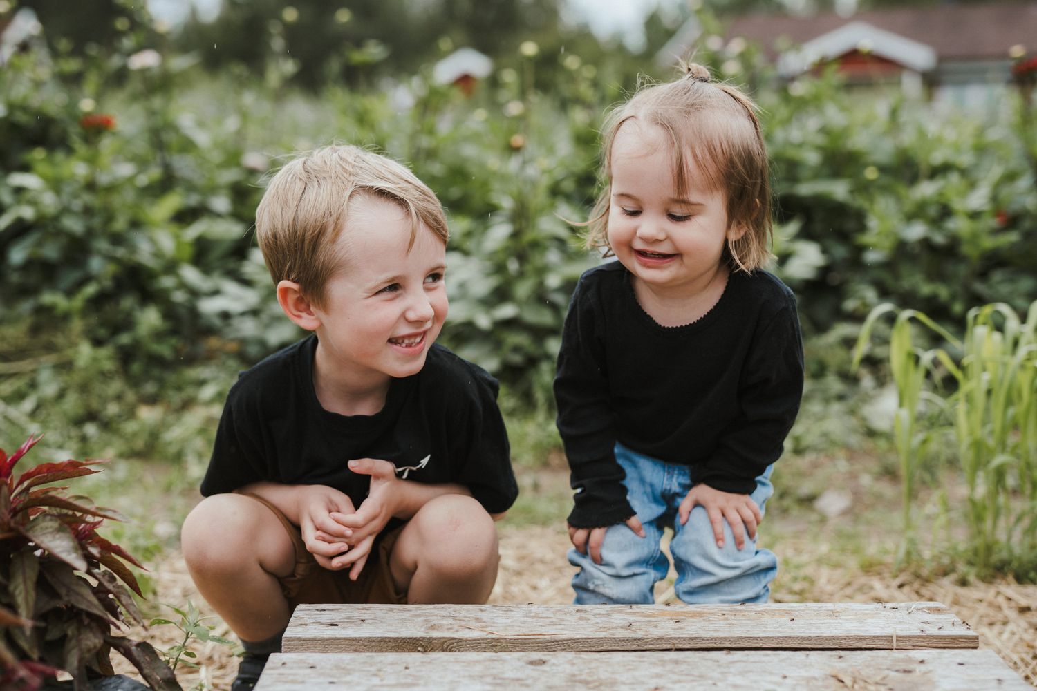 Två barn sitter på huk i en blomodling.