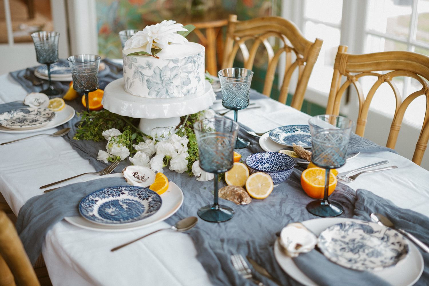 Elegant wedding table setting with blue china, citrus accents, and white floral cake centerpiece.
