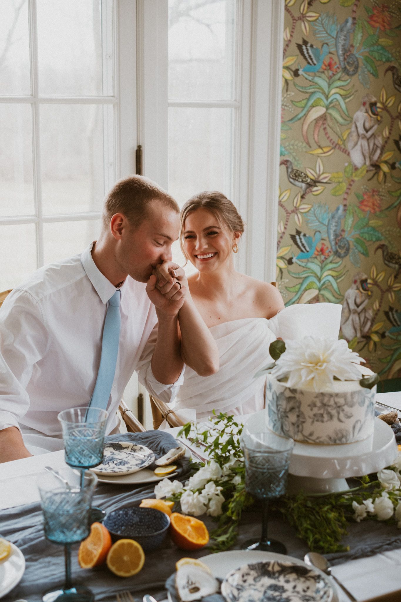 Wedding table scene with couple sharing intimate moment near decorative wallpaper.