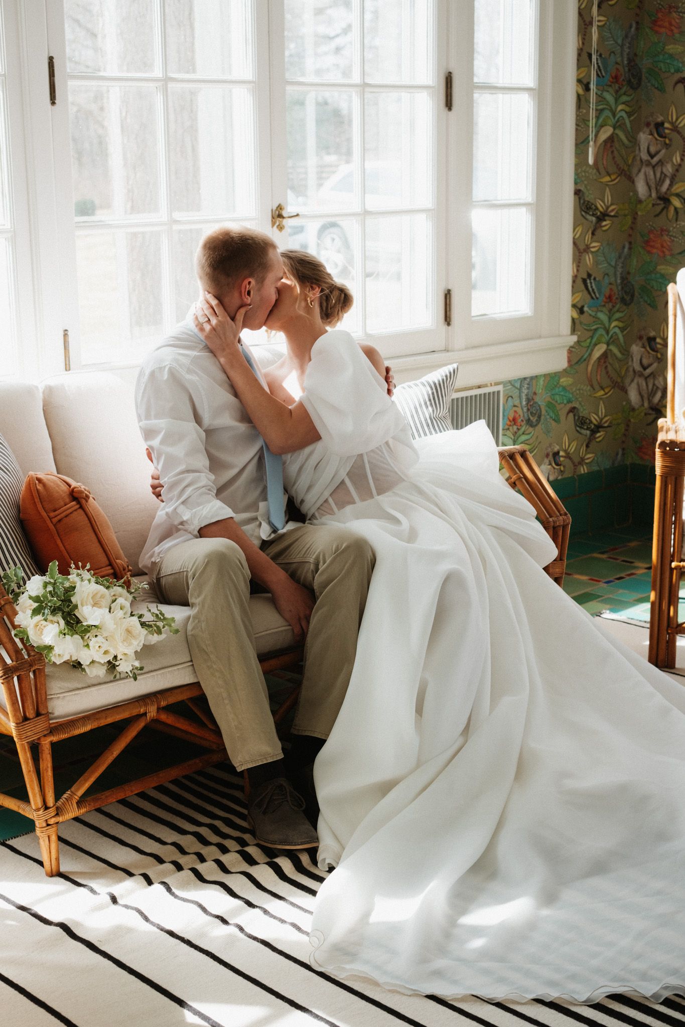Romantic wedding portrait on rattan chair against floral wallpaper.