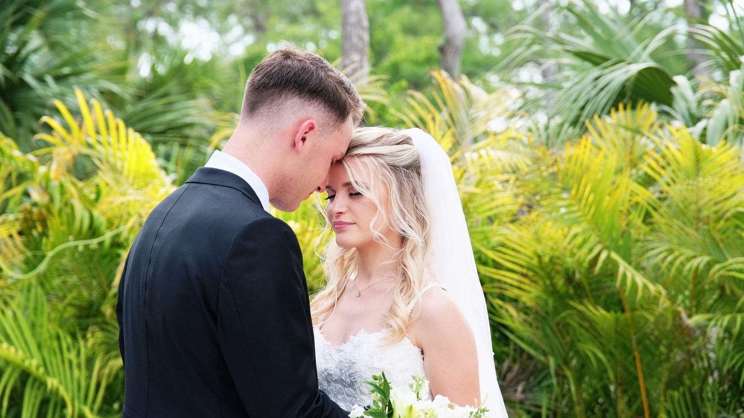A tender wedding moment set against a backdrop of vibrant tropical greenery.