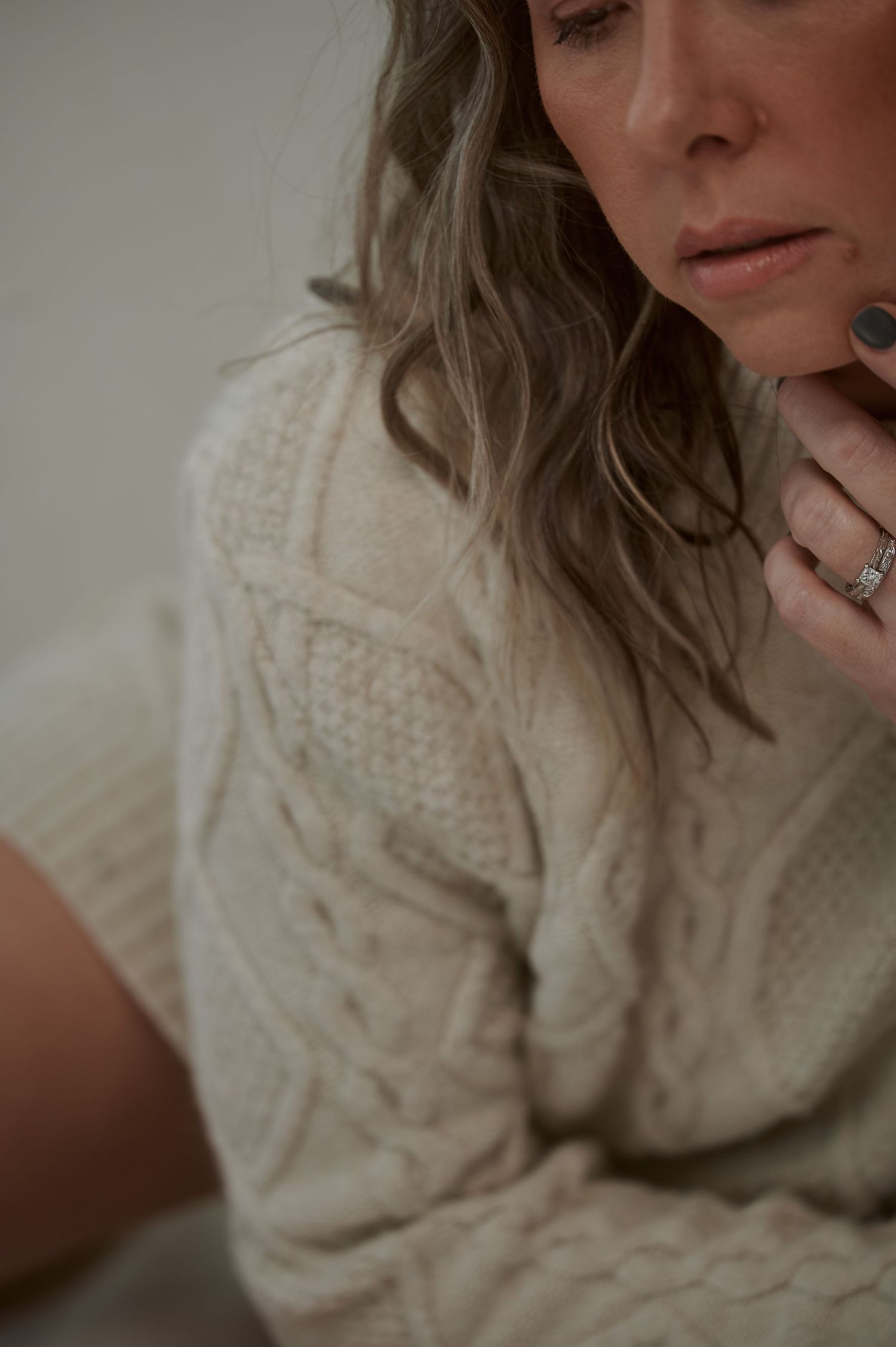 Detail shot of person in cable knit sweater with wavy hair and jewelry.