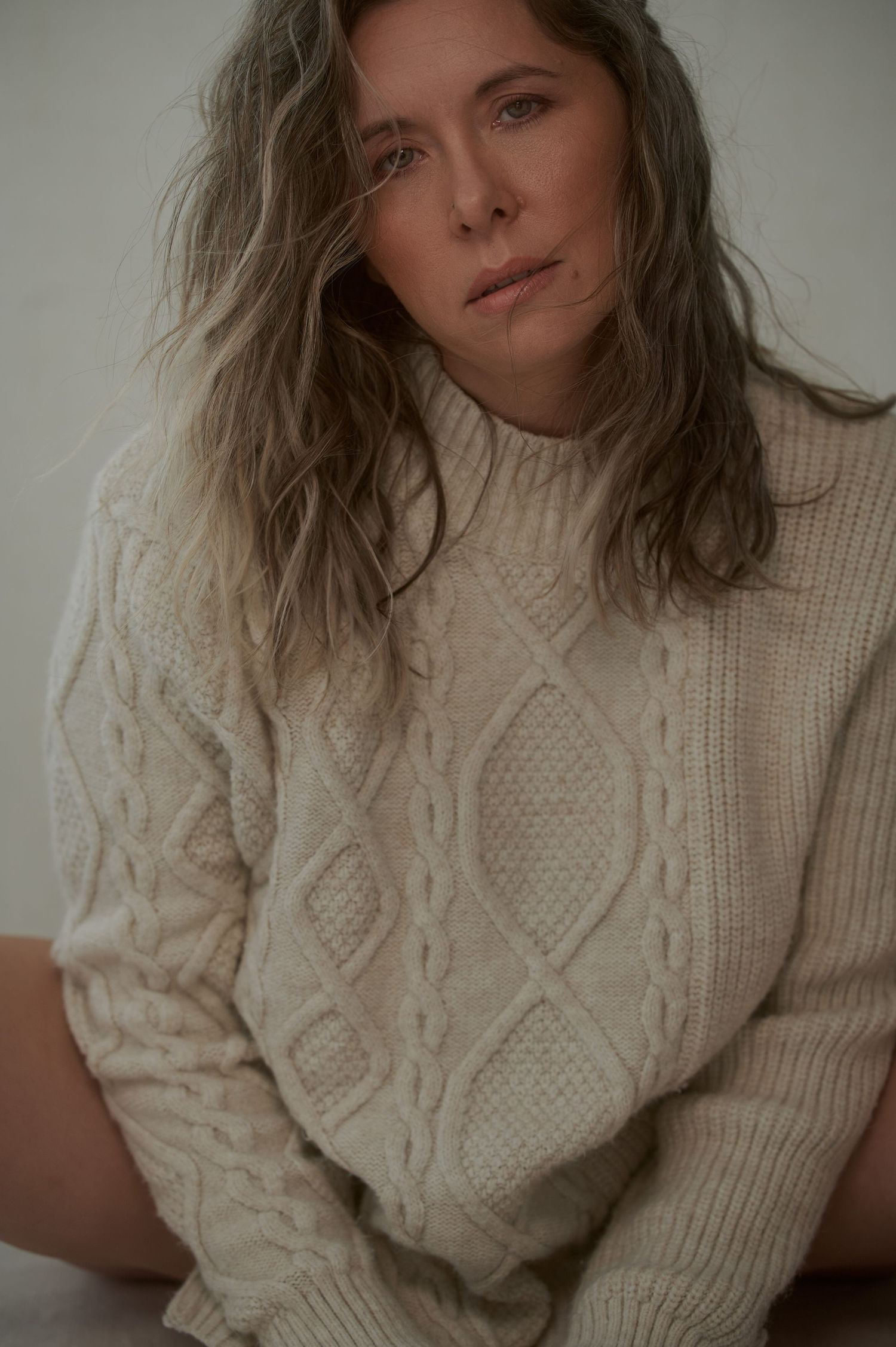 Cozy portrait in cream cable knit sweater against neutral background.