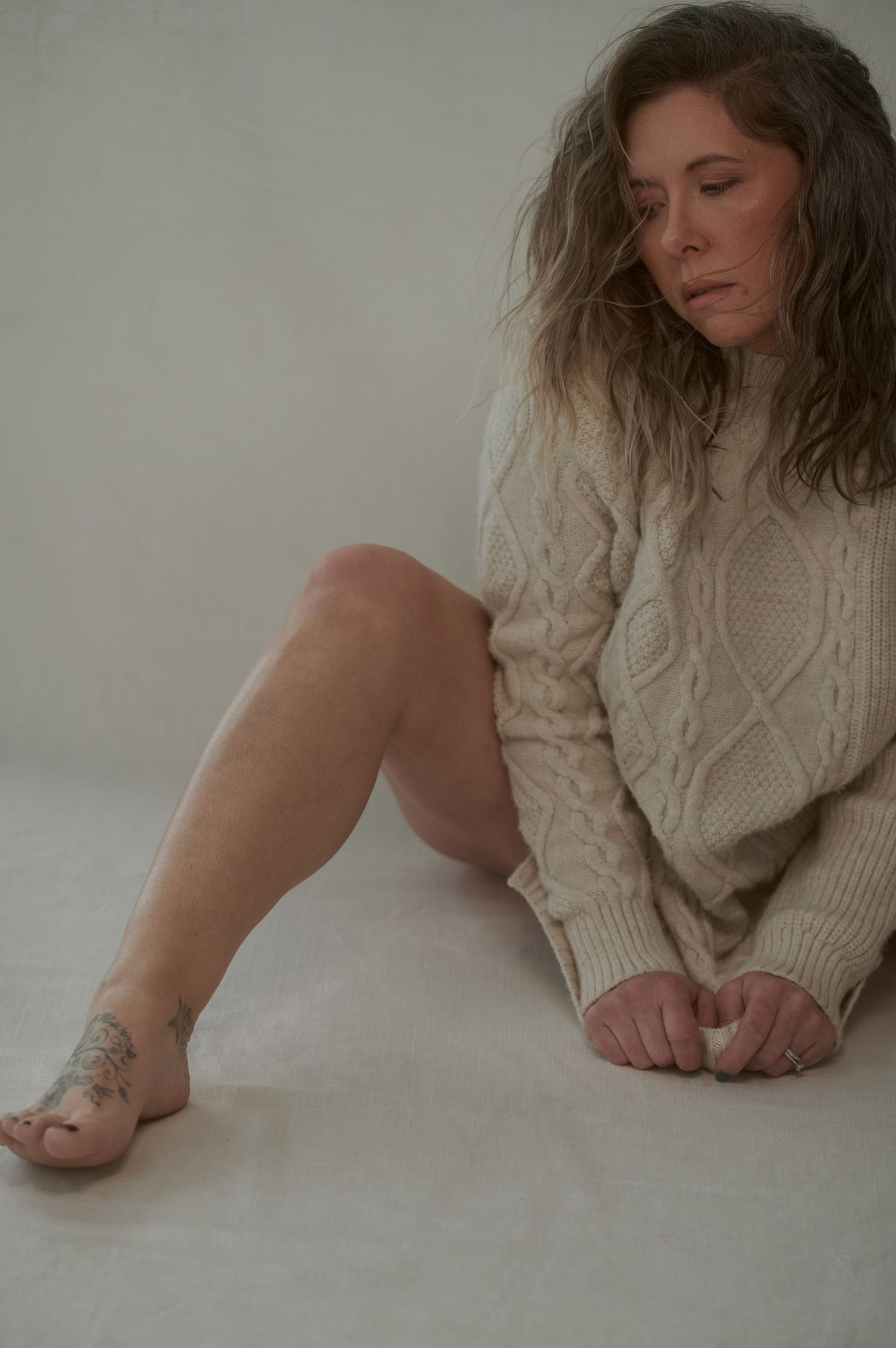Artistic portrait in cable knit sweater showing relaxed pose on light background.