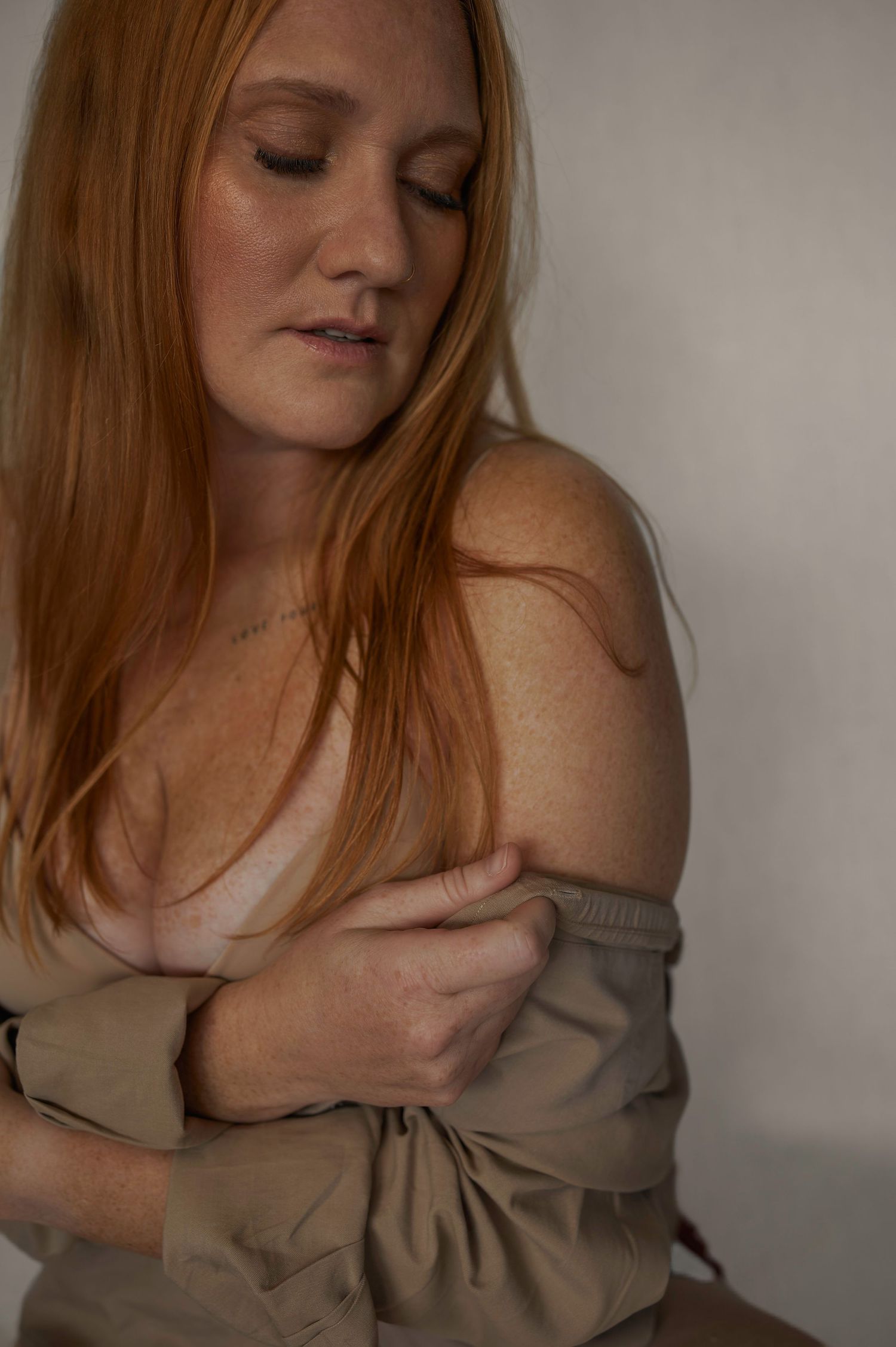 Artistic portrait featuring redhead in beige draped fabric against neutral backdrop.