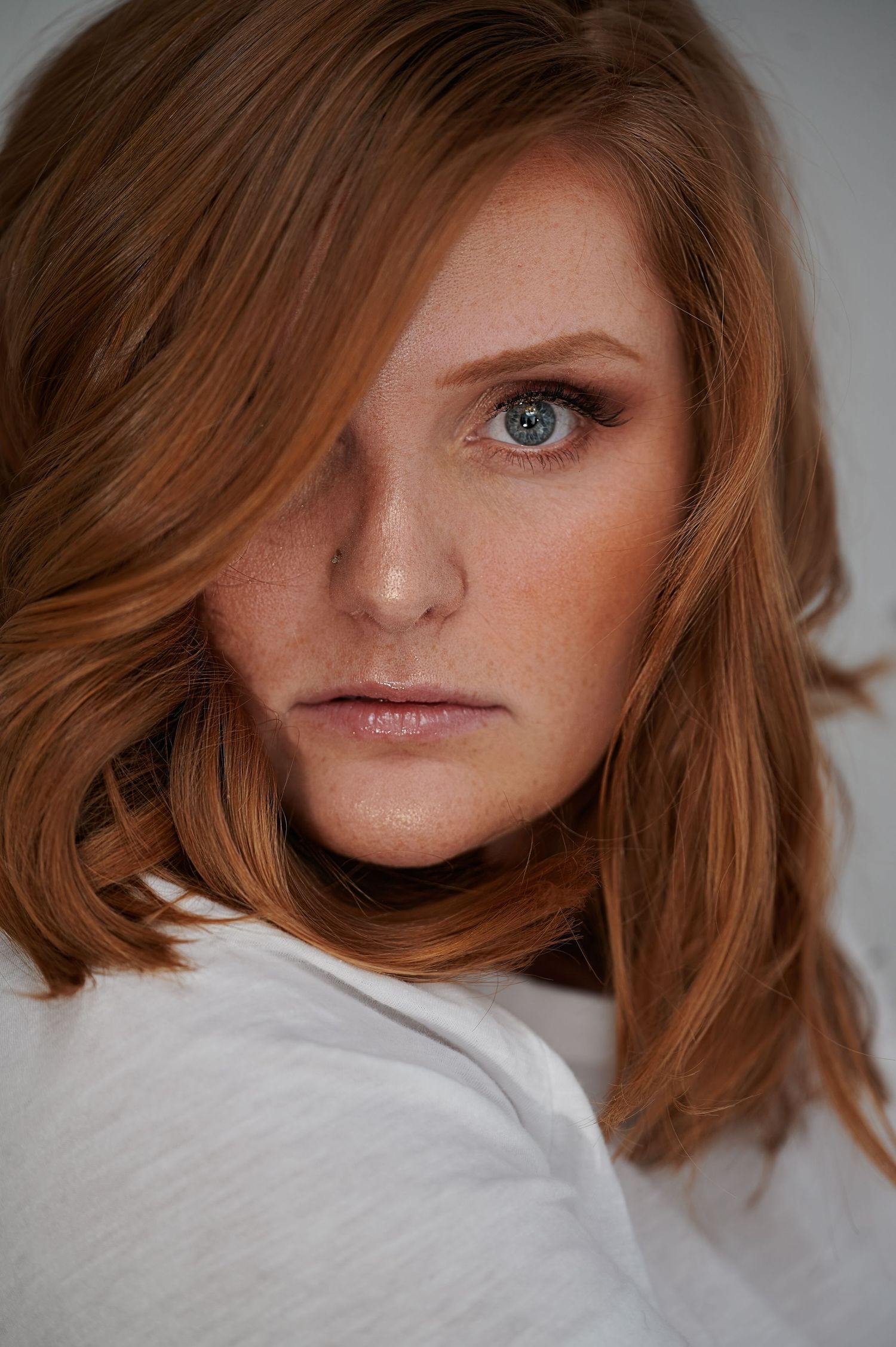 Portrait with soft lighting highlighting auburn hair and white top.