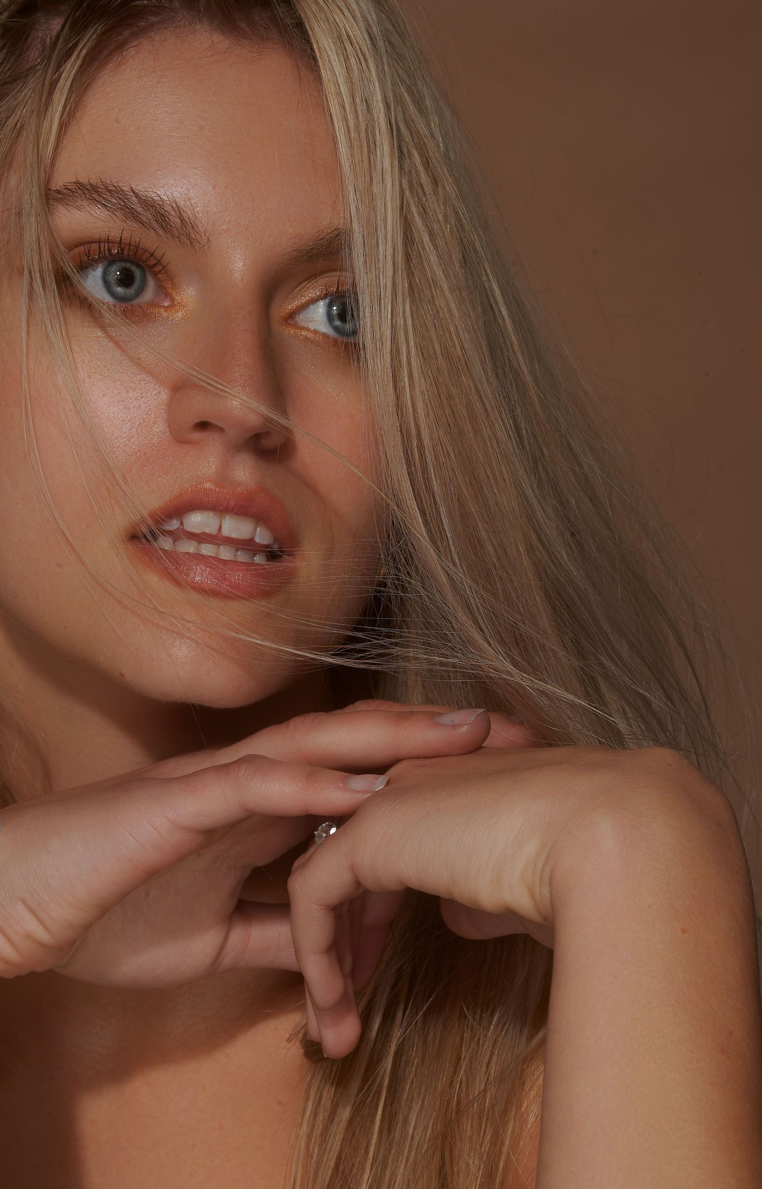 Beauty portrait with natural makeup and blonde hair against brown background.