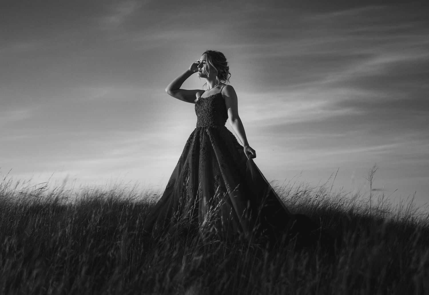 Silhouette of figure in flowing dress against dramatic sky on hilltop.
