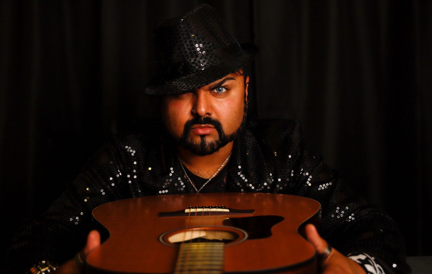 Musician in black cowboy hat holding acoustic instrument against dark background.