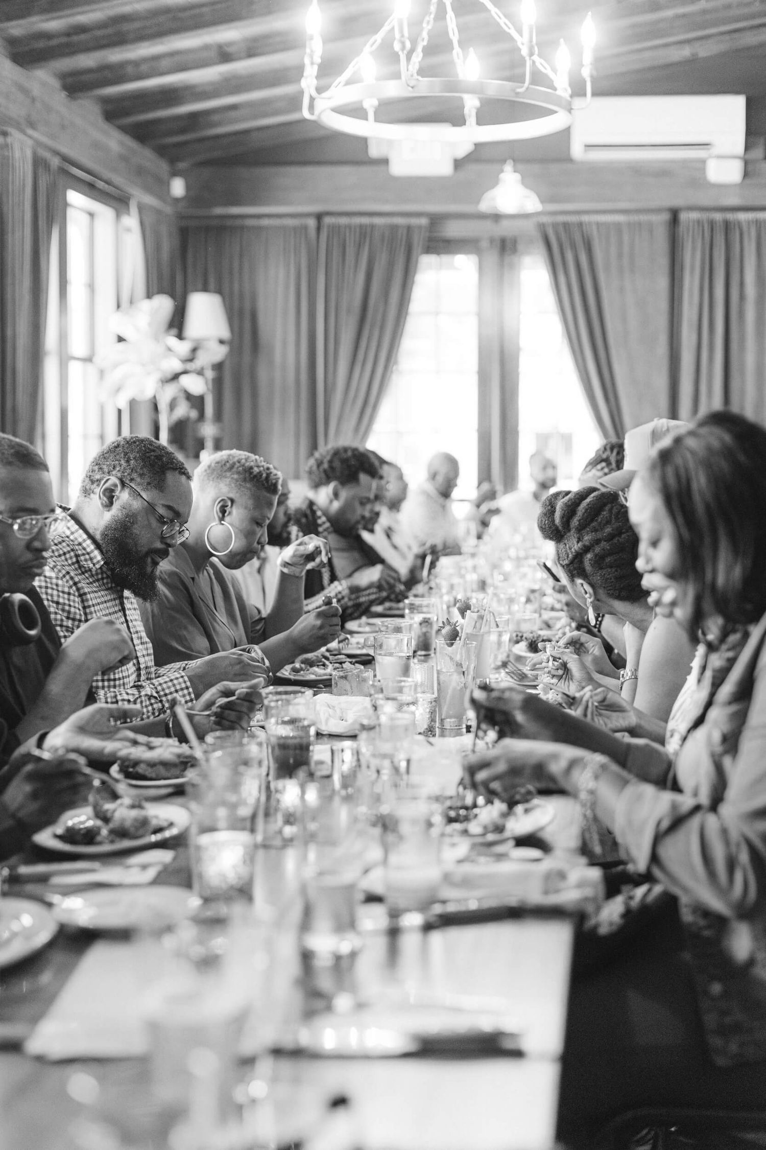 Black and white photo of diners enjoying a meal under elegant chandelier lighting.